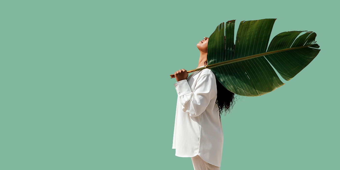 Young woman holding a palm leaf in front of a green background